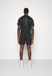 Svart atletisk ensemble bestående av en kortärmad tröja och shorts, båda med en slät yta. Tröjan har tre vertikala ränder på baksidan.