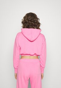 Felpa rosa corta con cappuccio e maniche lunghe, realizzata in un tessuto morbido. Presenta un orlo a coste e pantaloni della tuta abbinati con una tasca sul retro.