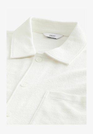 Valkoinen nappikauluspaita, jossa on tekstuuri, rento malli ja kaulus. Edessä on napit ja vasemmalla puolella tasku.