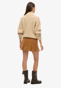 Beige ribstrikket striktrøje med høj hals, parret med en brun kordfløjl plisseret mini nederdel og sorte combat støvler med spænde detaljer.