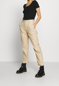 Black ribbed short-sleeve top, beige relaxed-fit trousers with side pockets, worn with black lace-up combat boots on a plain background.