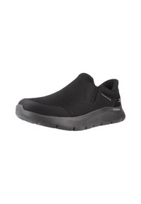 Zapato negro tipo slip-on con parte superior de malla texturizada y suela acolchada. Presenta una punta redondeada y sin cierres visibles. Diseño ligero.
