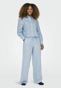 Camisa de botones azul claro con detalles de ojales, combinada con pantalones de pierna ancha a rayas en azul pastel y blanco. Tejido suave, ajuste relajado.
