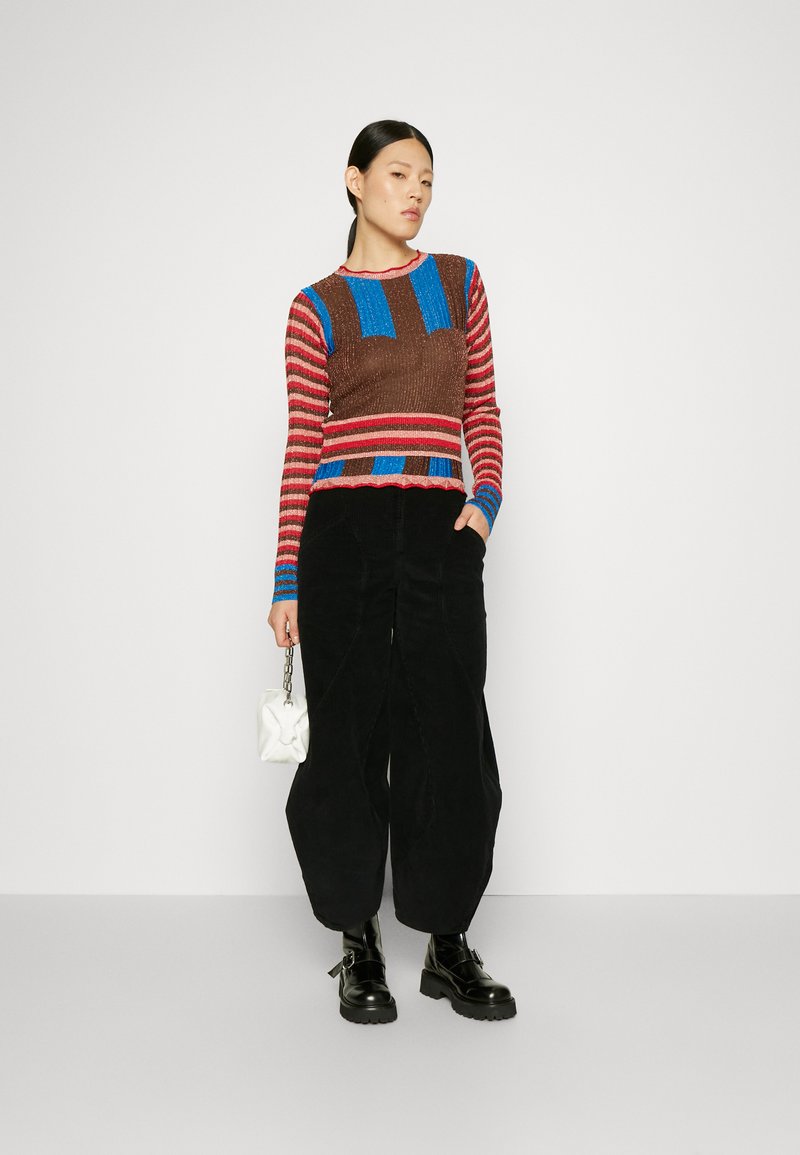 Pull en tricot multicolore avec des rayures marron, rouge et bleu ; associé à un pantalon large noir et des bottes noires à semelle épaisse. Petit sac à main blanc.