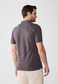 Dark gray short-sleeve polo shirt with a collar, featuring a smooth texture and side slits at the hem, worn with light-colored trousers.