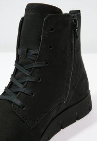 Bottine noire à cheville avec fermeture éclair latérale, lacets à l'avant et semelle épaisse, en daim.