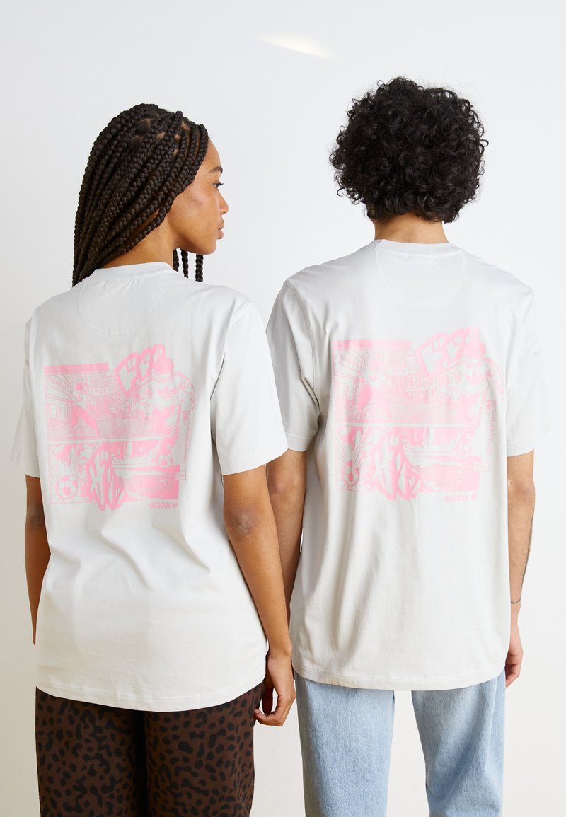 Ljust grå bomullströjor med korta ärmar, med en stor rosa grafisk design på baksidan. Tyget verkar mjukt med en avslappnad passform.