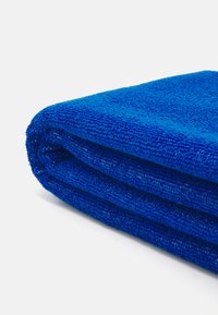 Modrá osuška z froté, poskladaná, s textúrovaným povrchom s slučkami a hladkým okrajom. Bohatá saturácia farby.