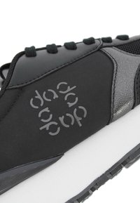 Zapatilla deportiva negra con una parte superior suave y un acento gris brillante, panel de malla texturizada y una entresuela blanca. Incluye logo de la marca en gris.
