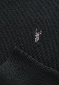 Schwarzer gestrickter Pullover mit einem geribbelten Muster. Hat ein kleines silbernes Hirsch-Emblem auf der Vorderseite. Die Bündchen verfügen über ein passendes geriffeltes Design.