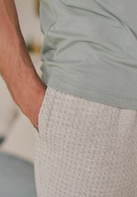 Helle grüne T-Shirt mit glatter Textur, kombiniert mit hellgrauen Shorts, die ein strukturiertes, waffelartiges Muster und eine Seitentasche aufweisen.