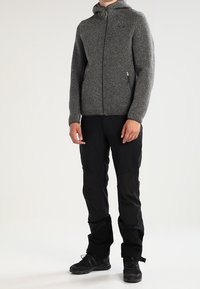 Szara dzianinowa kurtka zapinana na zamek z kapturem, w połączeniu z czarnymi spodniami i czarnymi butami. Wyróżniająca się faktura materiału oraz dopasowany krój.