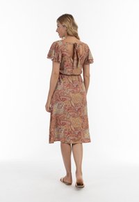 Šaty s paisley vzorem v červené a zlaté barvě, s jemnými rukávy a designem s klíčovou dírkou na zádech, doplněné dobře padnoucím pasem a středně dlouhým lemem.