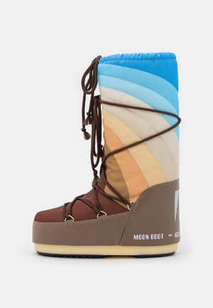Botte d'hiver haute avec des blocs de couleurs bleu, beige et marron, des lacets marron enroulés autour, et le logo "Moon Boot" sur le talon.