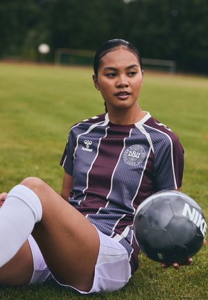 Maroon and blue striped soccer jersey with white accents, paired with white shorts. Player holds a black Nike soccer ball on grass.