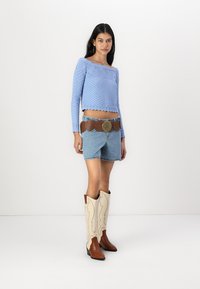 Ljust blått stickat cropped tröja med texturmönster, matchat med denimshorts, brunt läderbälte och krämfärgade cowboyboots med bruna detaljer.