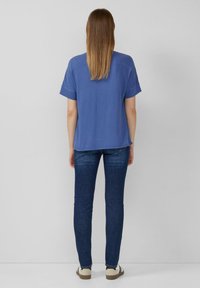 Niebieska koszulka z krótkim rękawem o luźnym kroju, zestawiona z ciemnoniebieskimi wąskimi dżinsami i jasnymi trampkami. Gładki wzór bez żadnych nadruków.