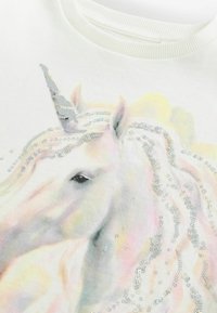 Witte sweatshirt met een kleurrijk eenhoornontwerp, versierd met glanzende zilveren pailletjes langs de manen en de hoorn, wat een textuureffect creëert.