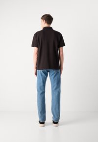 Svart polo-skjorte med korte ermer, kombinert med lyseblå jeans og svarte sneakers. Antrekket har en avslappet passform og enkelt design.
