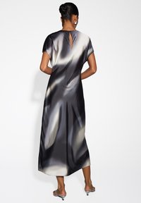 Frau trägt ein schwarz-weißes Satin-Midikleid mit kurzen Ärmeln und einem Rückenschlüssellochdetail, kombiniert mit silbernen Kitten-Heel-Sandalen.