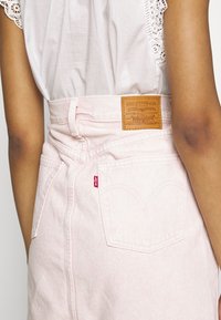 Gonna in denim rosa con vita alta, caratterizzata da una patch con logo in pelle, tasche posteriori e dettaglio con etichetta rossa. Tessuto liscio e silhouette aderente.