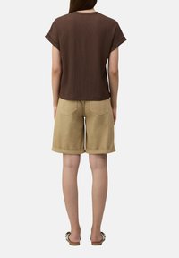 Bruine getextureerde top met korte mouwen, gecombineerd met beige shorts met omgeslagen mouwen en platte sandalen. Eenvoudig, casual ontwerp met duidelijke lijnen en minimale details.