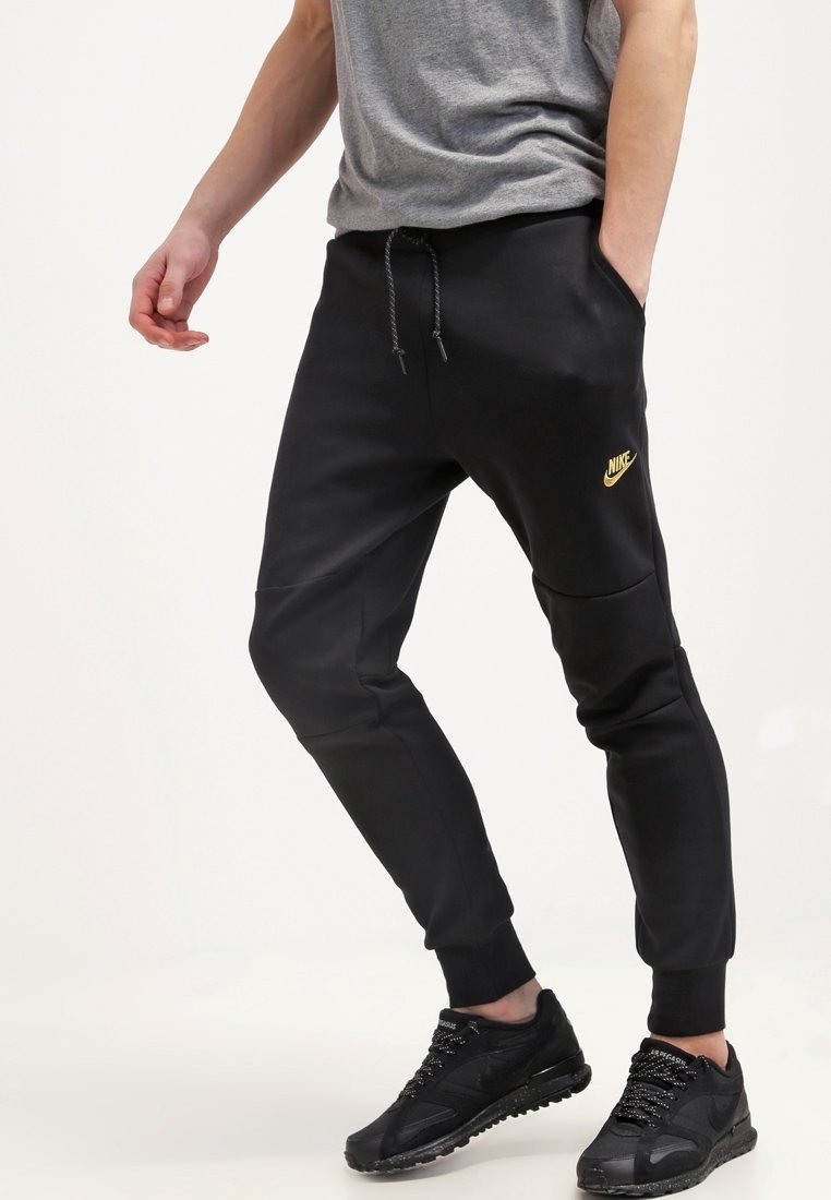 Black Nike joggers with elastic cuffs, featuring a gold logo on the thigh, made from a smooth fabric with a relaxed fit and drawstring waistband.
