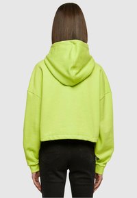 Hoodie accorciato in cotone di un vivace verde neon, con cappuccio, maniche ampie e una vestibilità comoda, abbinato a pantaloni neri.