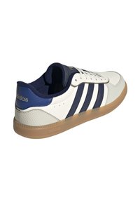 White sneakers with navy accents, featuring three stripes design, smooth leather upper, perforated sections, and a gum rubber sole.