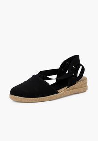 Espadrille negra con parte superior de lona, punta redondeada y suela de yute trenzado. Cuenta con tiras cruzadas en el tobillo y un tacón de cuña bajo.