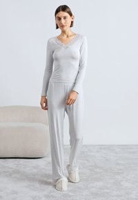 Svetlosivá súprava na pohodlie s dlhým rukávom a čipkovaným výstrihom, doplnená o elastické nohavice s rovnakým opaskom, spolu s krémovými papučami.