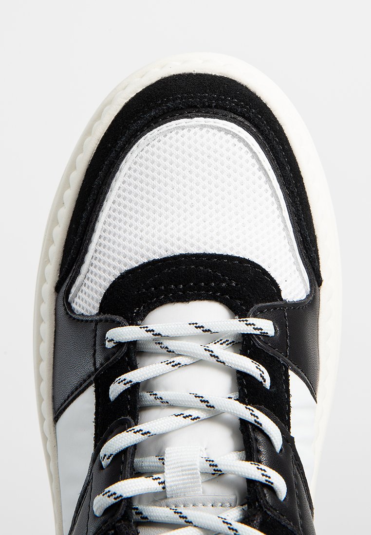 Schwarze Leder- und weiße Mesh-Sneaker mit einer strukturierten Oberseite, kontrastierenden Akzenten und flachen, gestreiften Schnürsenkeln. Runde Gummisohle.