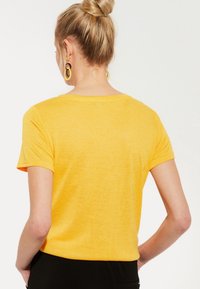 T-shirt jaune à manches courtes, en tissu léger, col rond, coupe décontractée. Détails de couture visibles aux épaules et aux ourlets.