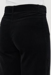 Black corduroy pants featuring a textured surface, a high waistband, and straight cut. Visible stitching along the seams, with no pockets shown.