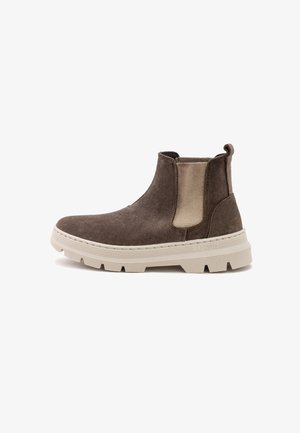 Barna velúr bokacsizma bézs elasztikus oldalsó panelekkel, vastag fehér gumi talppal, és hátsó húzófüllel a könnyű felhúzás érdekében.