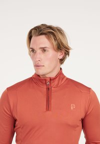 Rode long sleeve pullover met een halve rits kraag, zachte textuur en een klein logo op de borst; aansluitend ontwerp met gestikte accenten op de schouders.