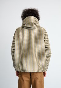 Hettejakke med et gult og hvitt vertikalt stripemønster, laget av lett materiale, med justerbar hem og avslappet passform.