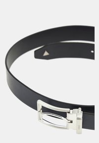 Zwarte leren riem met een gladde textuur, voorzien van een zilveren metalen gesp met een rechthoekige uitsparing en pin afsluiting.