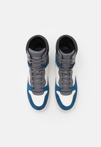 Vysoké tenisky vyrobené z šedé kůže, s modrými semišovými akcenty a bílým textilním tělem. Obsahují šedé tkaničky a logo na kotníku.