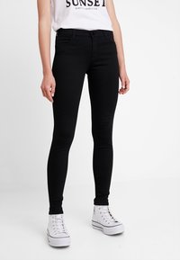 Jeans skinny negros de denim con textura suave. Presenta un diseño clásico de cinco bolsillos, trabillas para cinturón y cierre de cremallera.