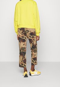 Sudadera amarilla brillante de manga larga, acompañada de pantalones beige con un patrón mármol multicolor y zapatillas amarillas con acentos negros.