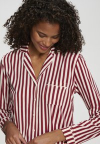 Svītraina pogājamā krekla ar sarkaniem un baltiem svītrām, ar izdurtu apkakli, garām piedurknēm un krūšu kabatu. Mīksts kokvilnas materiāls.