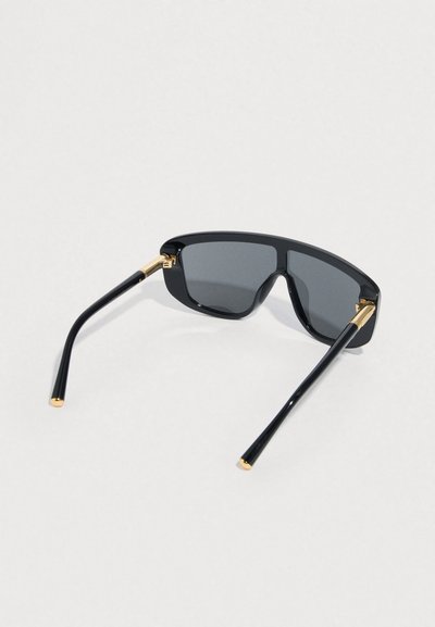 Fekete napszemüveg szürke lencsékkel, szögletes kialakítással, fényes kerettel, arany díszítéssel a zsanéroknál, valamint keskenyedő fekete szárakkal.