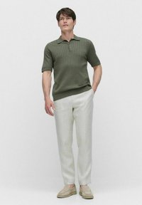 Olivgrön kortärmad polo skjorta med ribbad textur, matchad med ljusbeiga byxor och beige slip-on skor. En enkel och modern design.