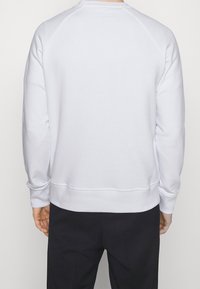 Sudadera blanca con cuello redondo, mangas raglán y puños acanalados. Presenta una textura suave y un diseño simple y minimalista.