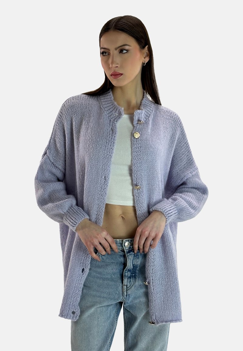 Cárdigan de punto lila con cuello redondo, con botones dorados, mangas holgadas y un corte relajado, sobre una blusa blanca.