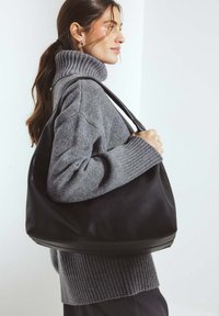 Black leather shoulder bag with a smooth texture, large silhouette, and a wide strap, paired with a cozy gray ribbed turtleneck sweater.