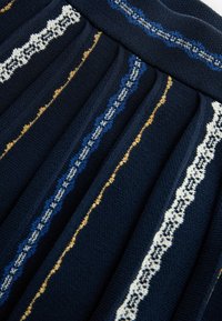 Tessuto blu navy con pieghe che mostrano motivi decorativi in blu, oro e bianco. Il materiale presenta una finitura a maglia texture.