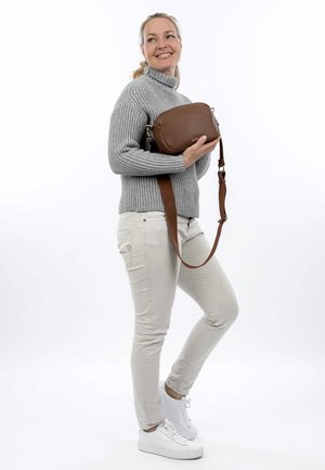 Brown leather crossbody bag with adjustable strap, rectangular shape, textured surface, and silver hardware accents. Worn by a person.