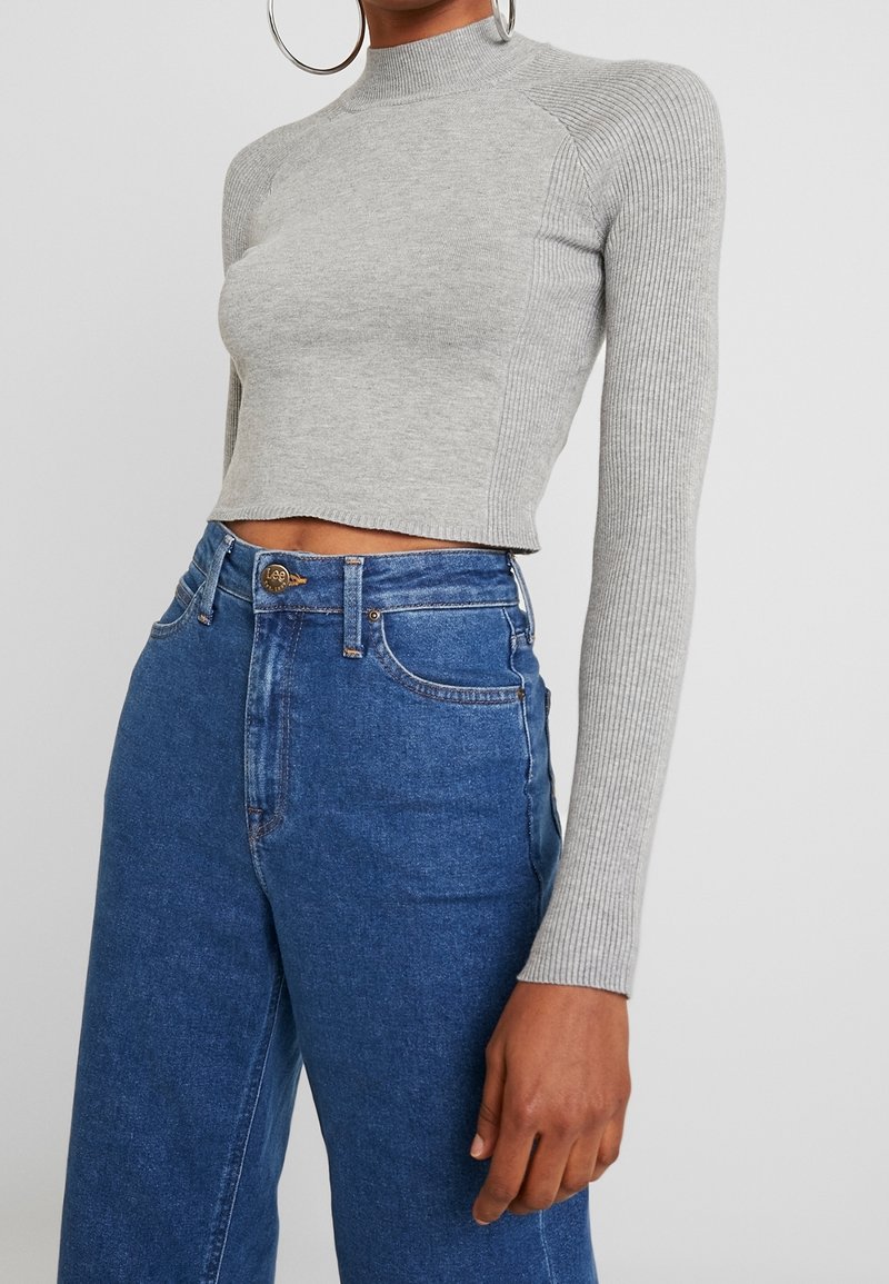 Top de punto gris acanalado, cropped, de manga larga con cuello alto, combinado con jeans de mezclilla azul de cintura alta que presentan un diseño clásico de botones y bolsillos.